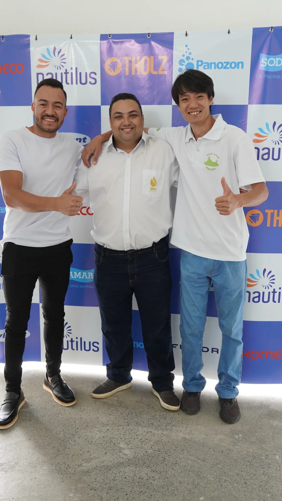Três convidados posando em frente ao painel dos patrocinadores